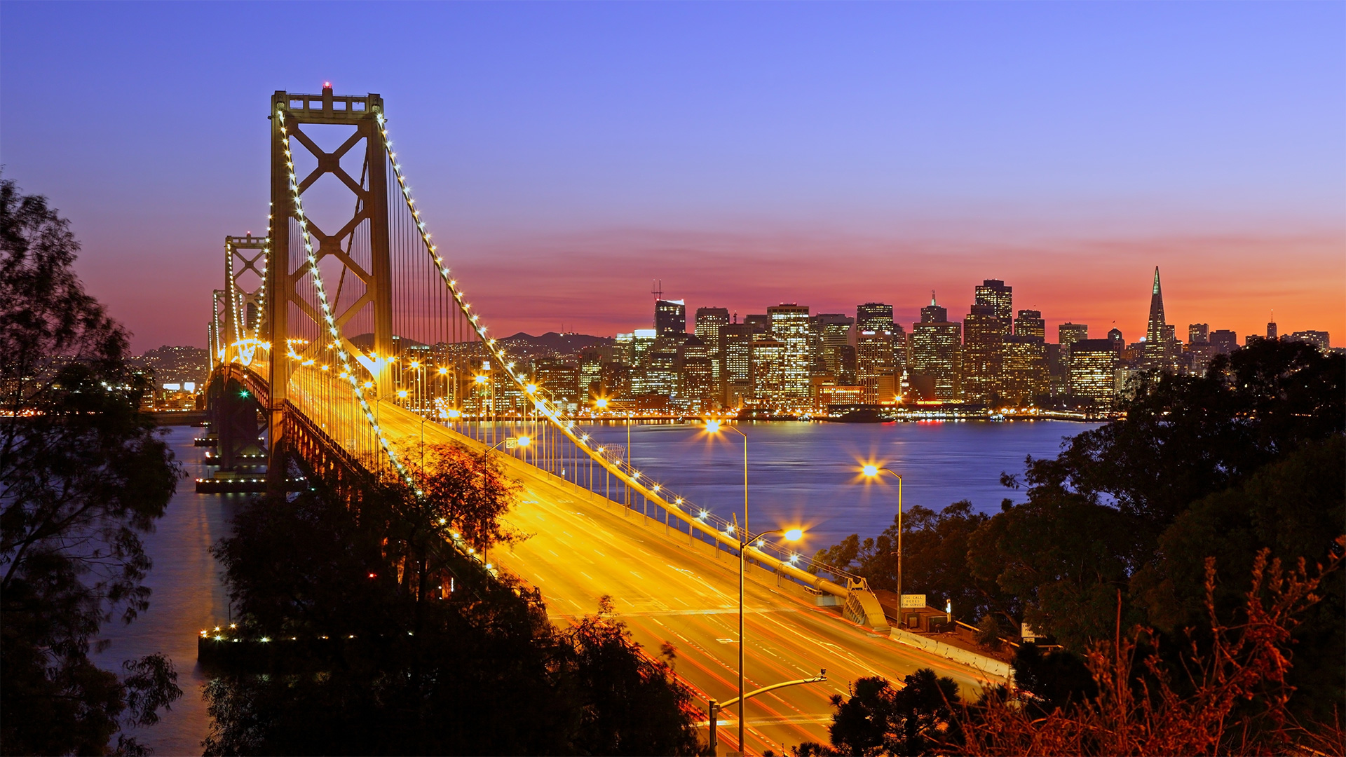 Night view of the San Francisco skyline at sunset with the Bay Bridge lit up.