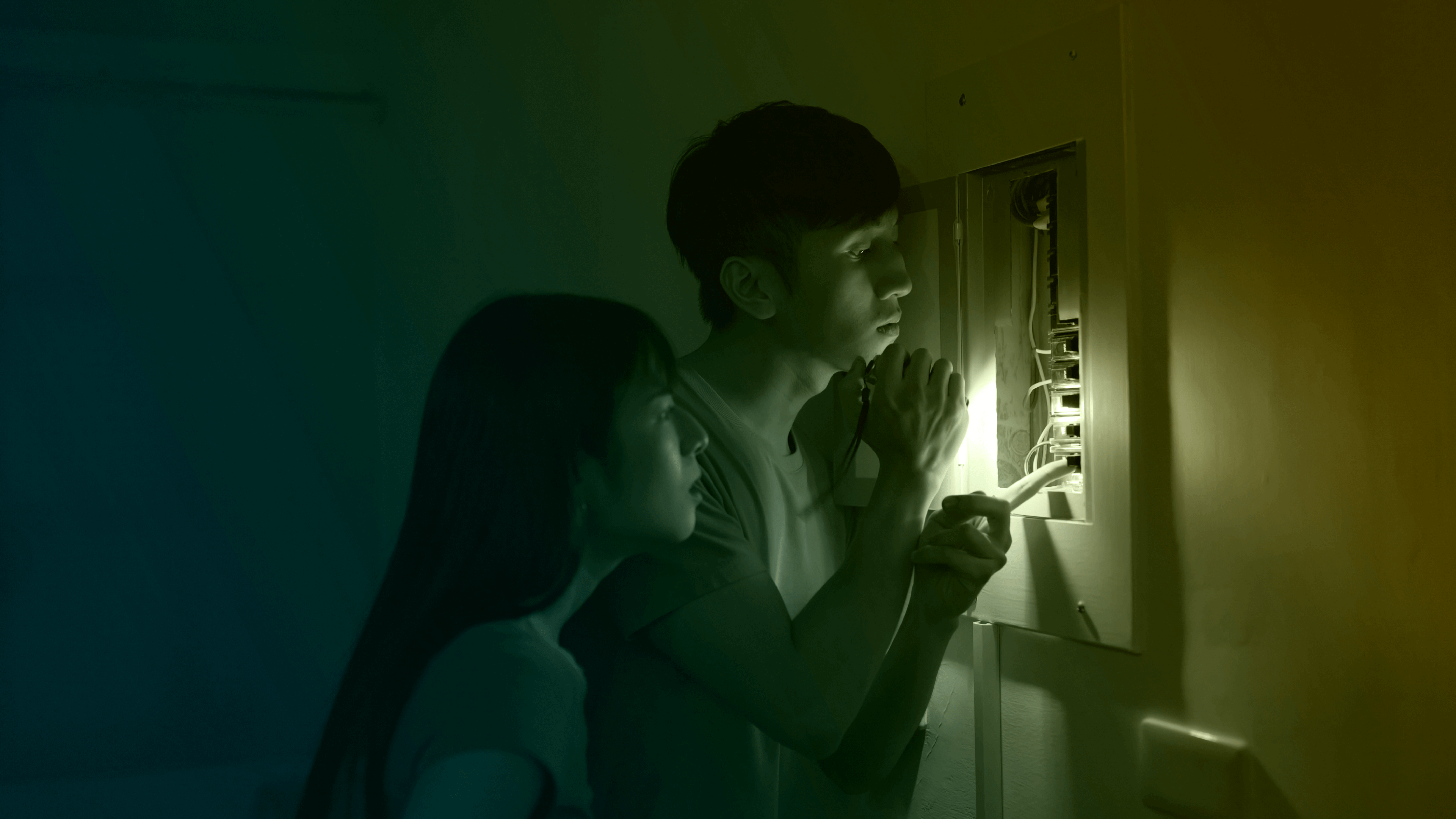 Couple inspecting breaker box with flashlight in blackout.