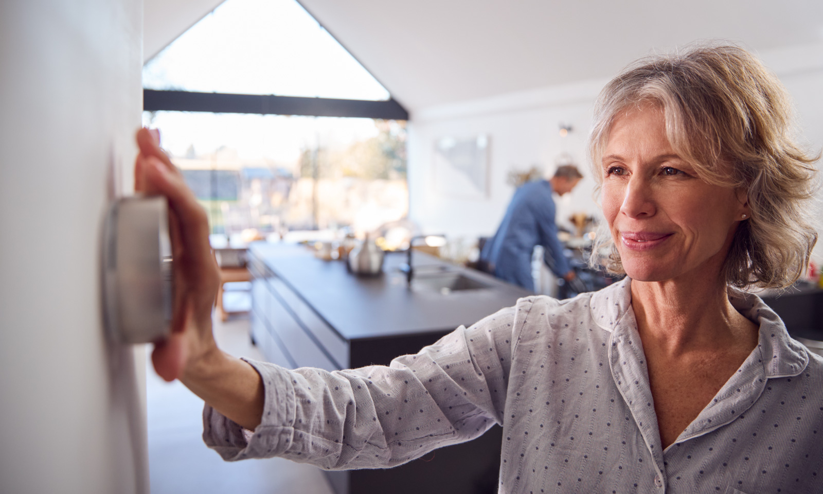 Woman adjusting home thermostat to save electricity