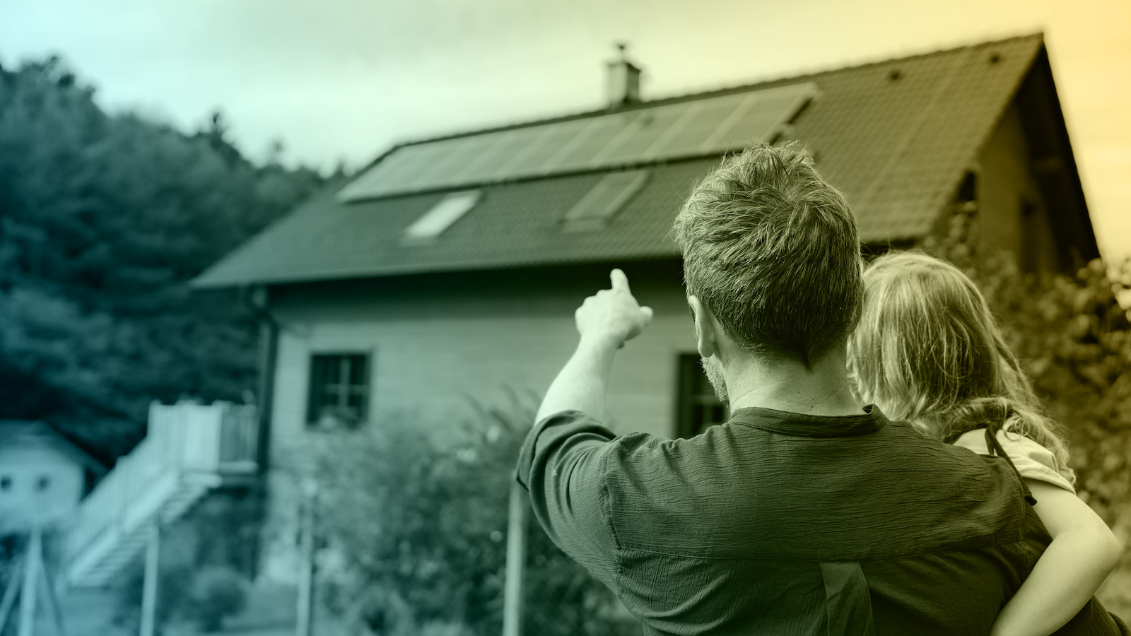 Father holding child while pointing at rooftop solar panels on a home, representing family investment in clean and sustainable energy.