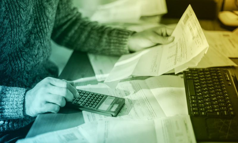 Person calculating electricity bills using a calculator and laptop, illustrating energy costs and budgeting for utility payments.