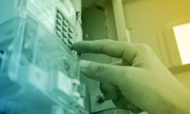 Hand pressing buttons on an electricity meter, symbolizing prepaid energy usage and home power monitoring.