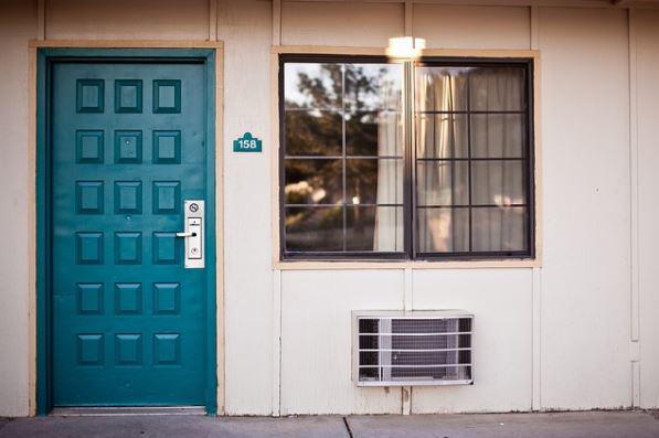 A teal-colored exterior door next to a window and a wall-mounted air conditioning unit outside a home or apartment.