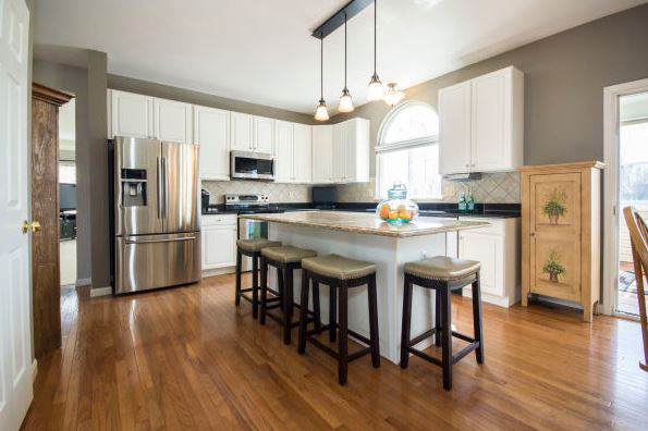 A bright modern kitchen with white cabinets, stainless steel appliances, and a wooden floor centered around a large island with stools.