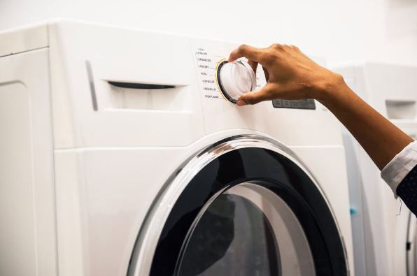 A person adjusts the settings on a front-loading washing machine in a laundry area.